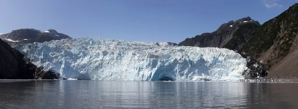Wide tidewater face of Aialik Glacier meeting calm water under a clear sky