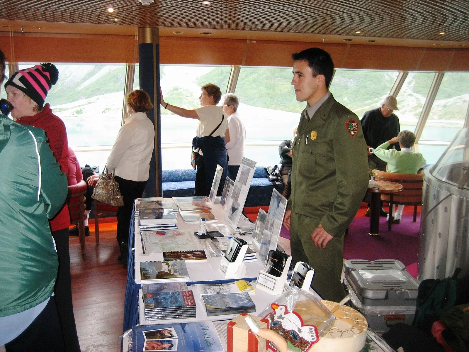 A National Park Service ranger at an information table aboard a cruise ship in Glacier Bay, a highlight of an Alaska cruise for seniors, while passengers look out the windows