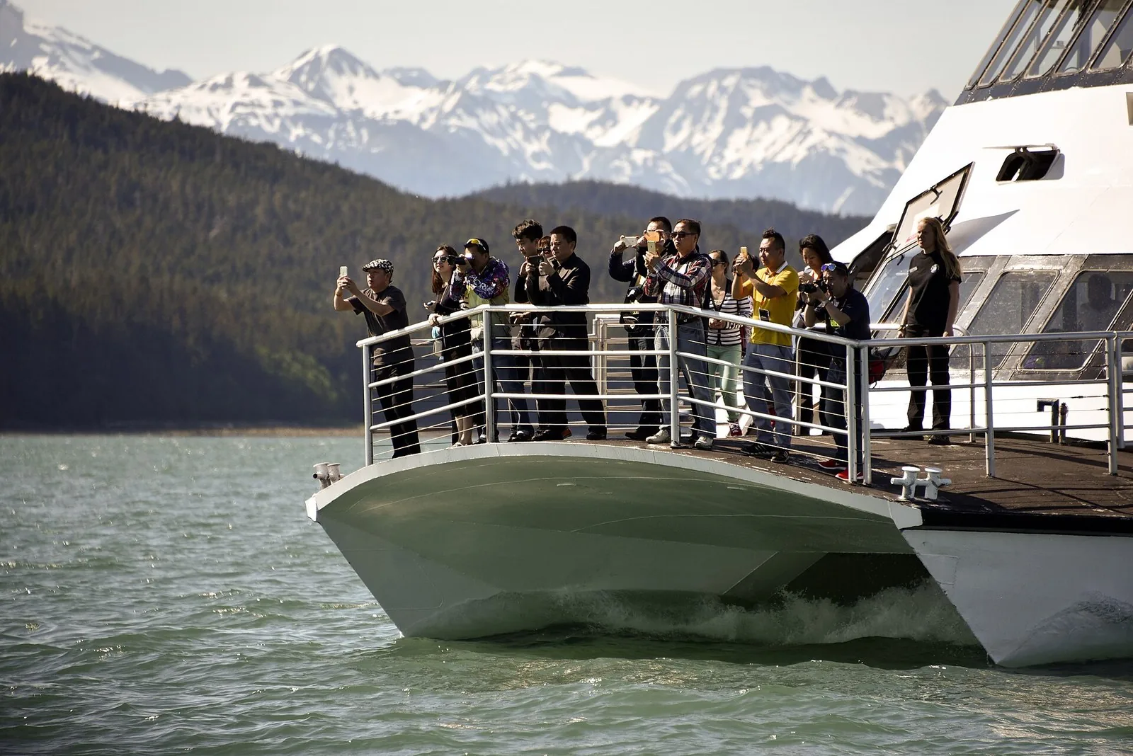 Whale-watching passengers in jackets, hats and layers photographing from a boat's bow near Juneau, dressed from an Alaska cruise packing list