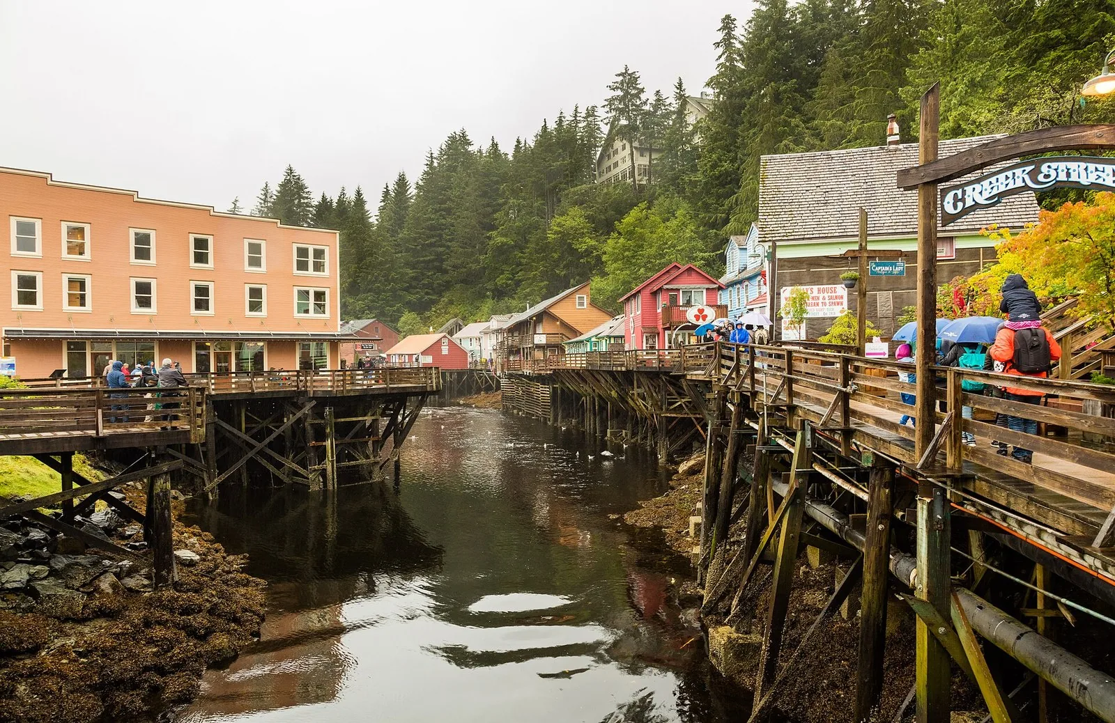 Visitors with umbrellas and rain jackets on Ketchikan's Creek Street boardwalk above the creek, a rainy port day behind many Alaska cruise tips