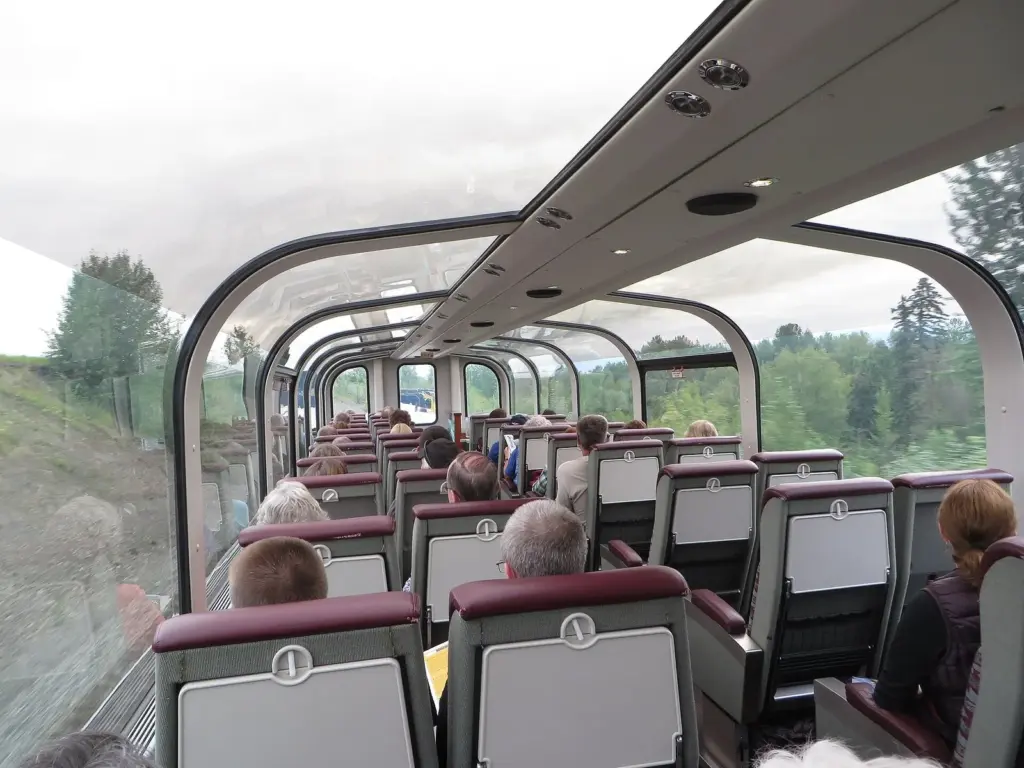 Passengers seated under the glass roof of an Alaska Railroad GoldStar dome car rolling past green forest