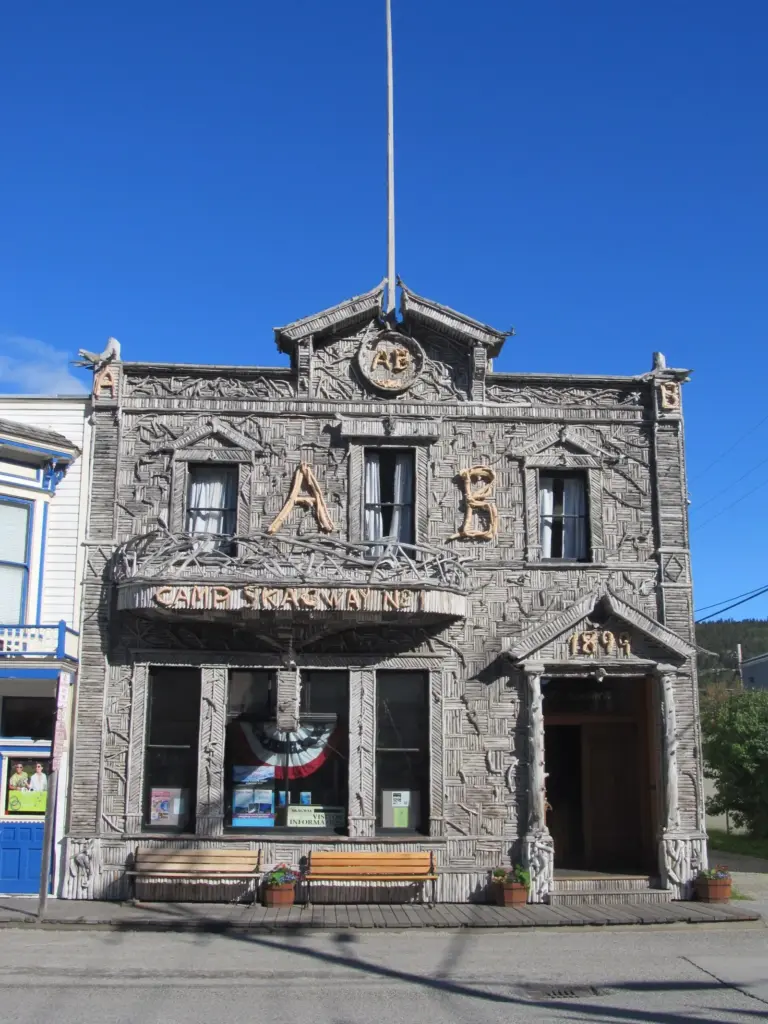 The Arctic Brotherhood Hall in Skagway, its facade covered in patterns of silver-gray driftwood, with benches and passers-by on the boardwalk