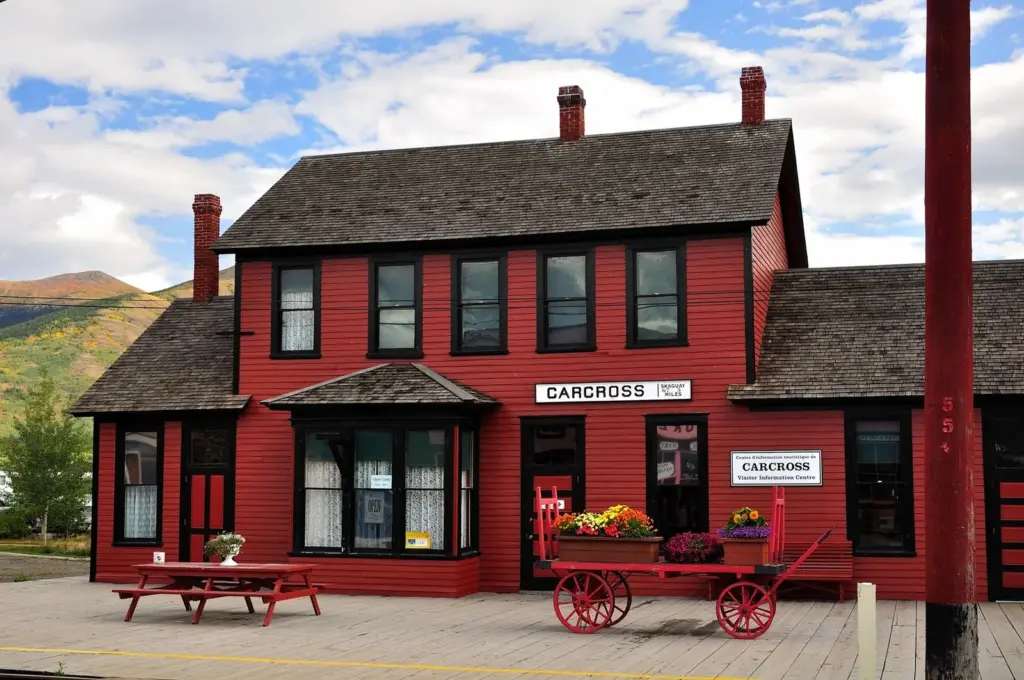 The red two-story Carcross railway depot with a flower-filled cart and picnic tables on its wooden platform