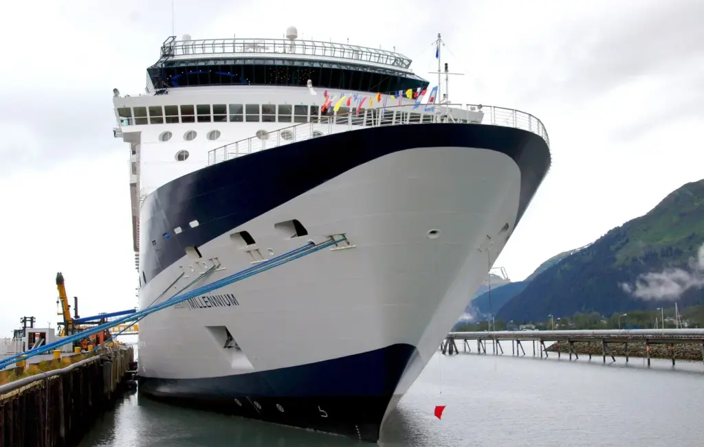 The bow of Celebrity Millennium tied up at a Seward dock with green mountains behind