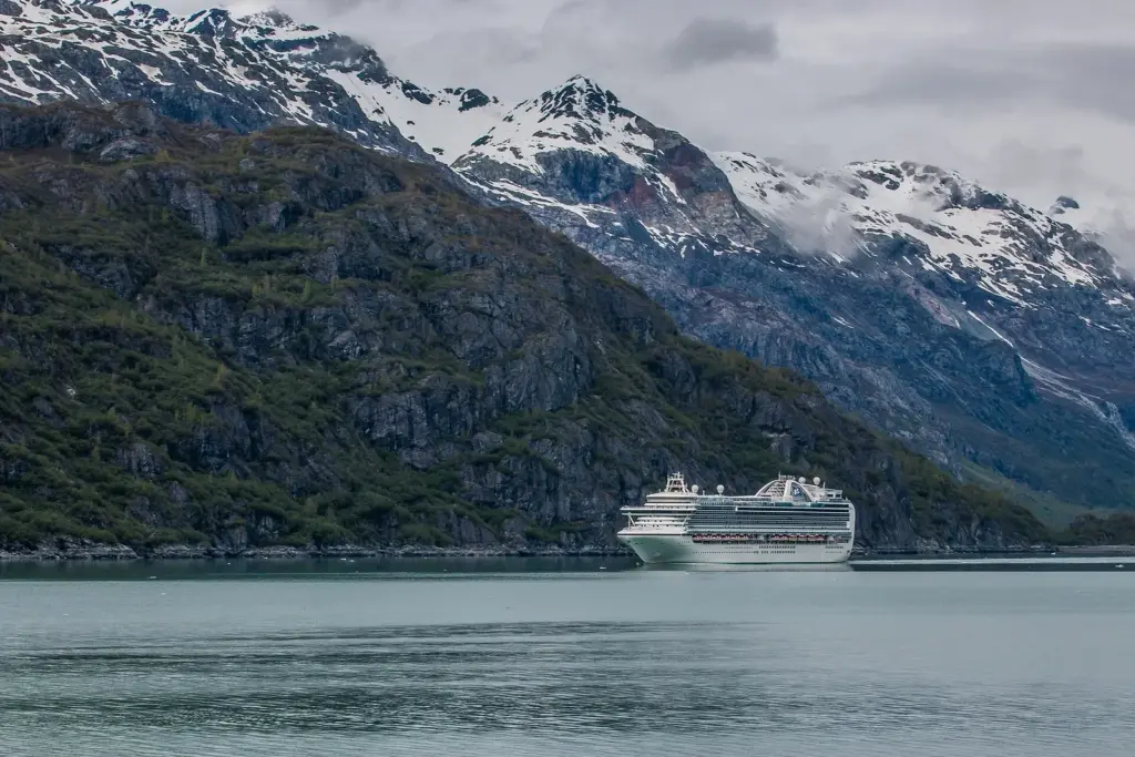 A large cruise ship dwarfed by snow-streaked mountains in Glacier Bay National Park, photographed from a second cruise ship