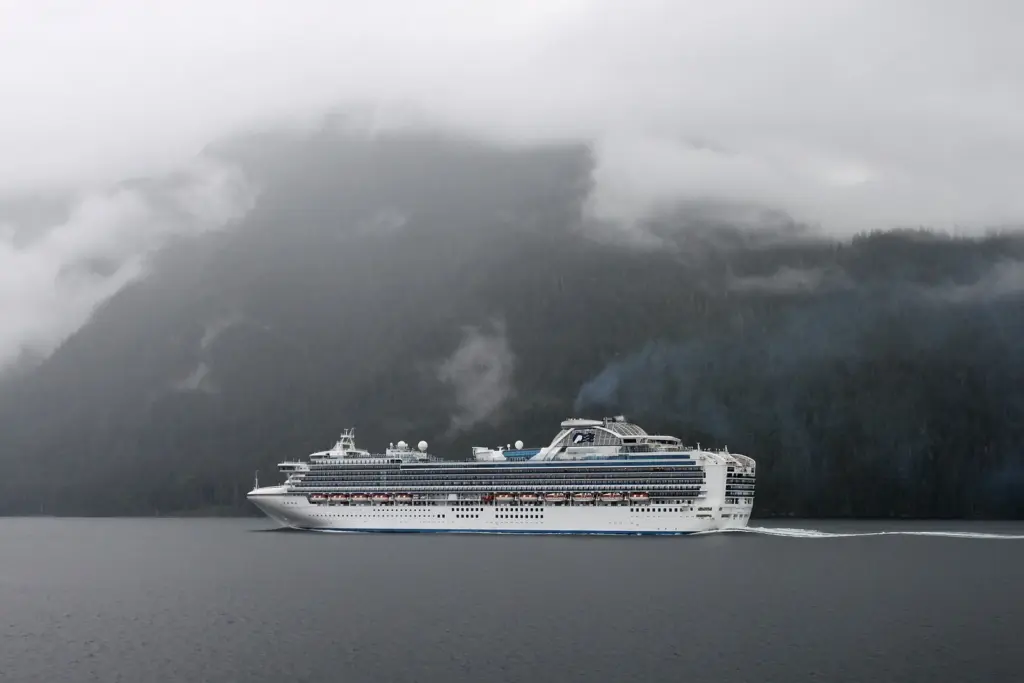 A large cruise ship sailing through a misty, forested channel of the Inside Passage in British Columbia