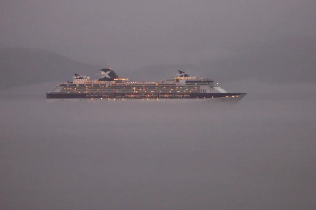 A cruise ship with its lights on sailing through evening mist in the Inside Passage northwest of Ketchikan