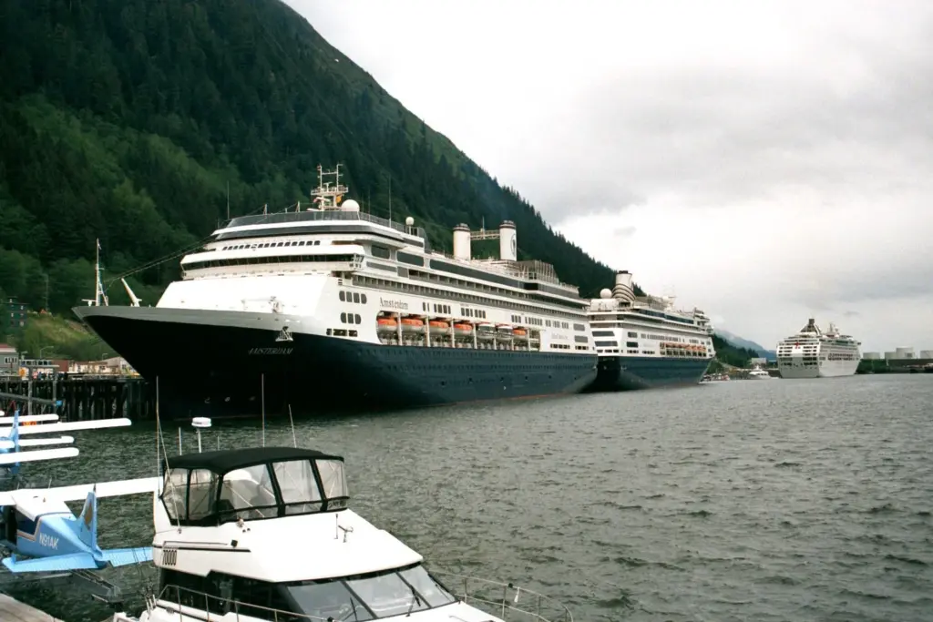 Several large cruise ships docked in a row along the Juneau waterfront below a steep forested mountain