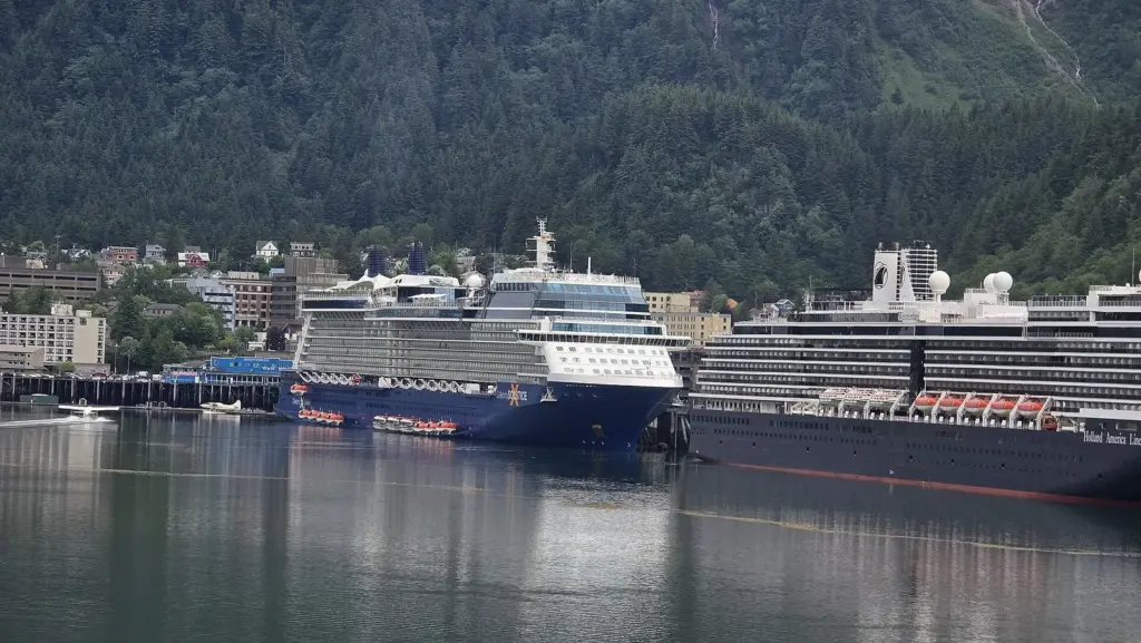 Two large cruise ships docked in Juneau below forested slopes, their balconies facing the channel