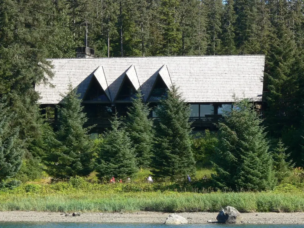 Shingled roof and dormer windows of the lodge among spruce trees above the shore
