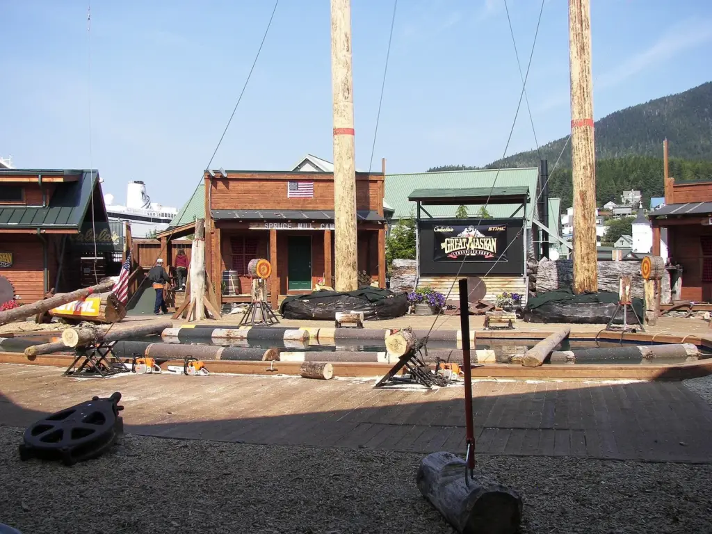 The open-air arena of the Great Alaskan Lumberjack Show in Ketchikan, with tall climbing poles, log piles and a covered grandstand