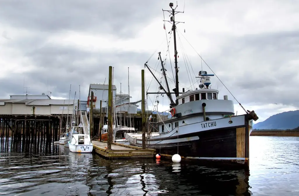 Wooden fishing boat moored at a Hoonah dock beside buildings on pilings