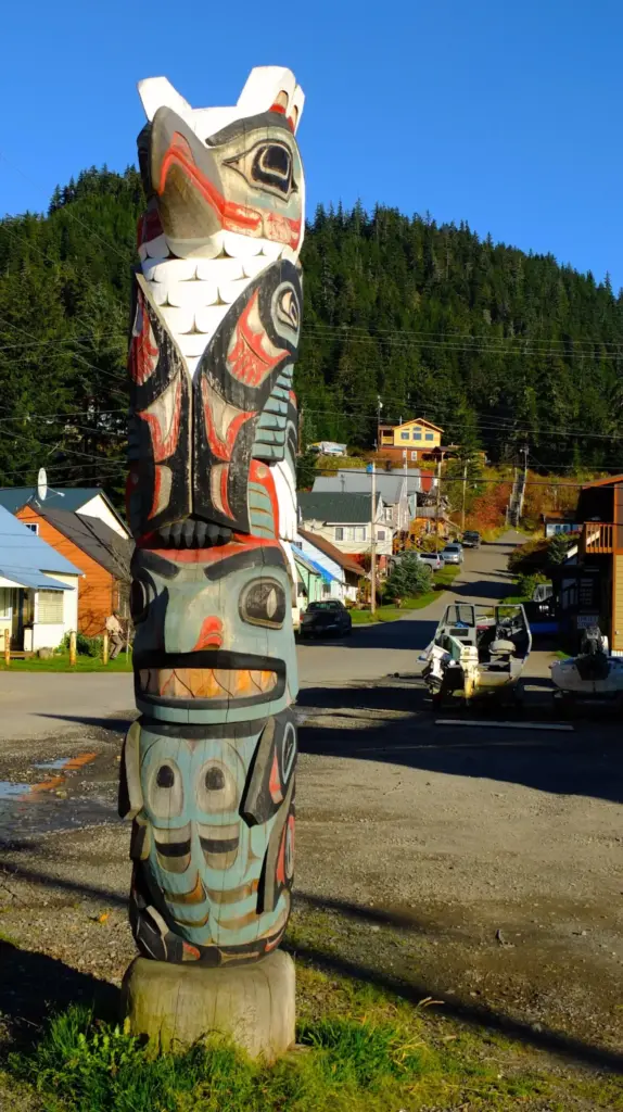 Painted totem pole beside a residential street in Hoonah under a blue sky
