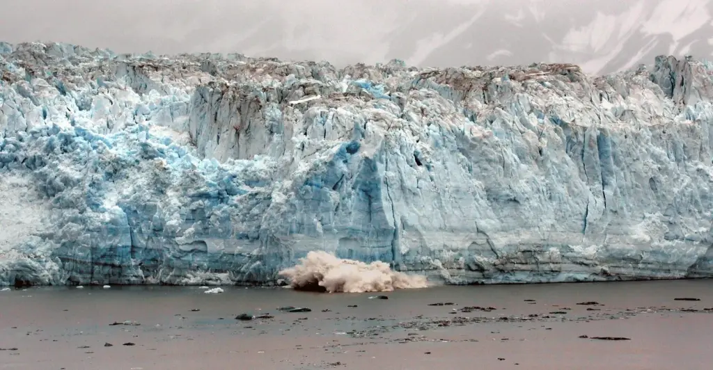 A slab of ice crashing into the sea from the blue, fractured face of Hubbard Glacier