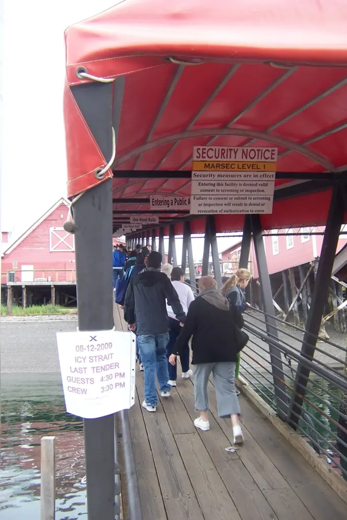 Cruise passengers walking along a covered wooden walkway toward the red cannery buildings