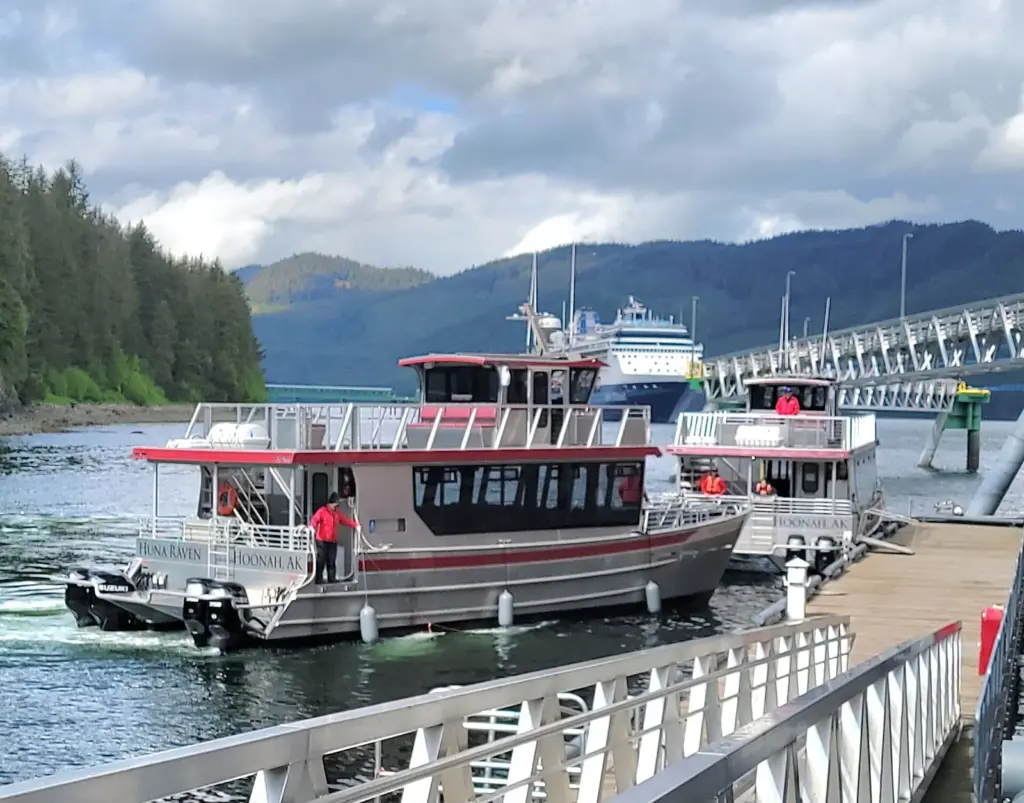 Two whale-watching boats at a floating dock with a cruise ship moored at the long pier behind