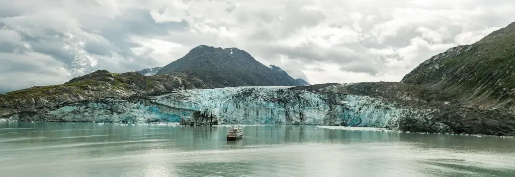Blue ice face of Lamplugh Glacier above gray water with a small boat in front