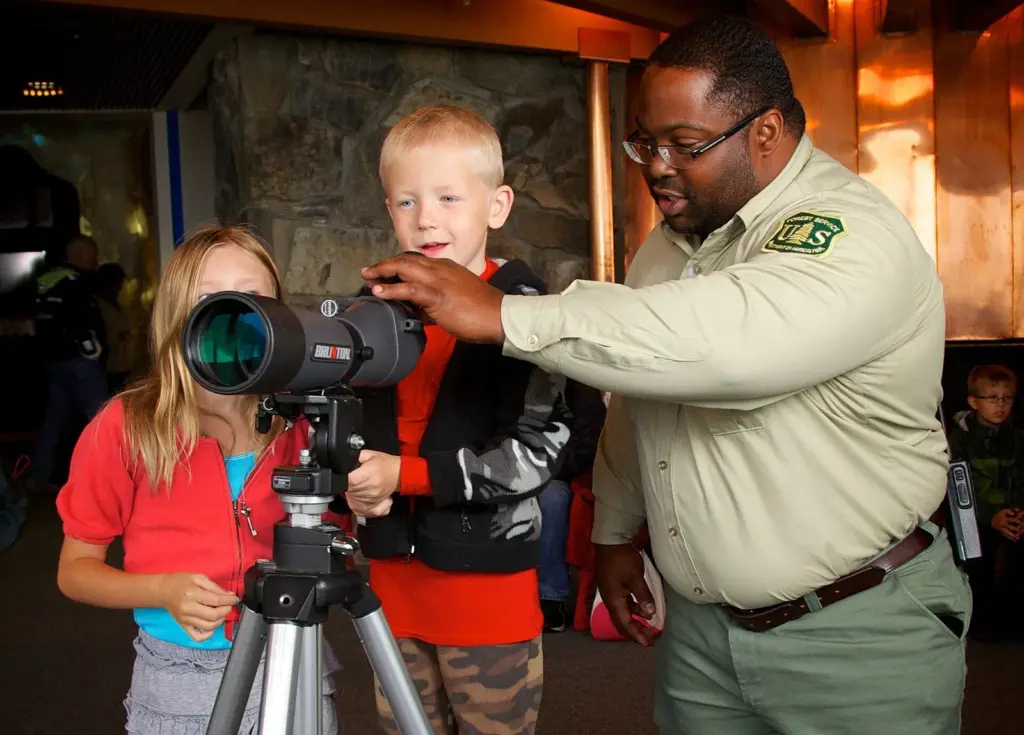 Forest Service guide helping two children look through a spotting scope at the Mendenhall Glacier visitor center