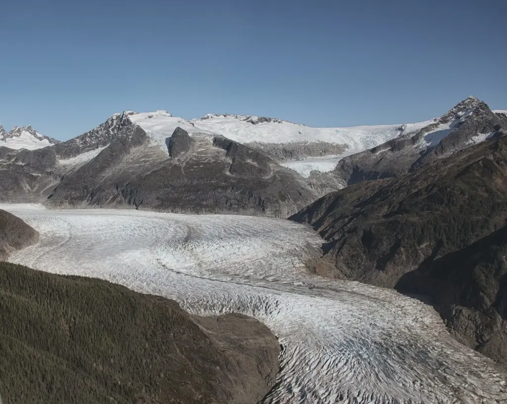The long, crevassed tongue of the glacier curving between mountains, seen from high above, with a side basin and a hanging glacier