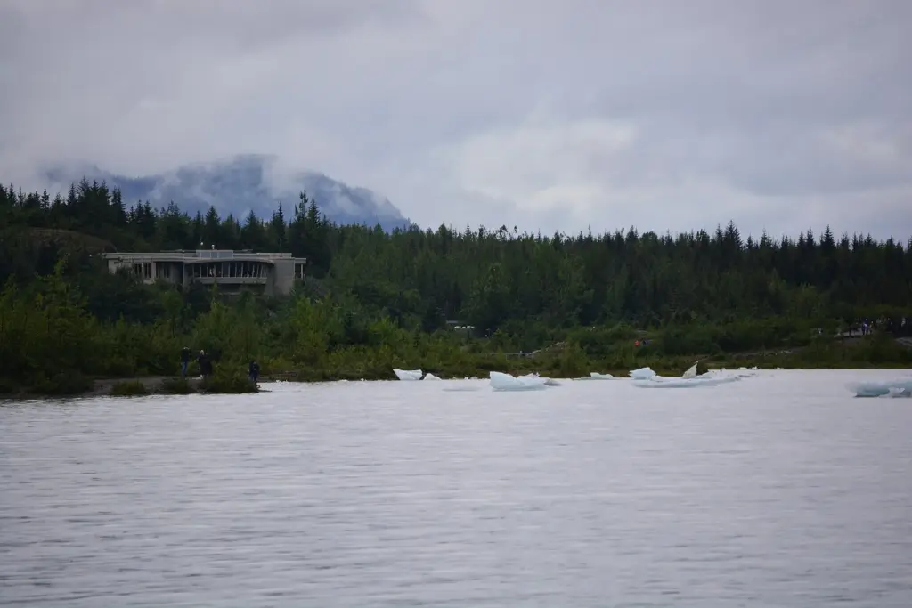 The low, curved visitor center on a forested rock knob above the lake, with small icebergs floating in front