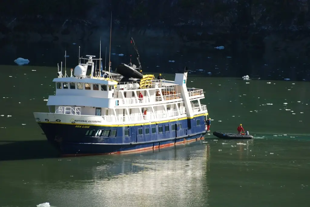 Lindblad's blue-hulled National Geographic Sea Lion idling in green water with a Zodiac alongside and floating ice nearby