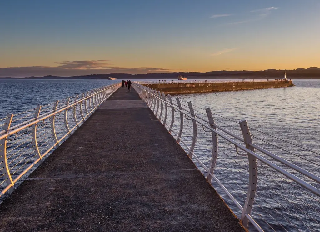 Long concrete breakwater walkway with railings stretching out to a lighthouse at sunset