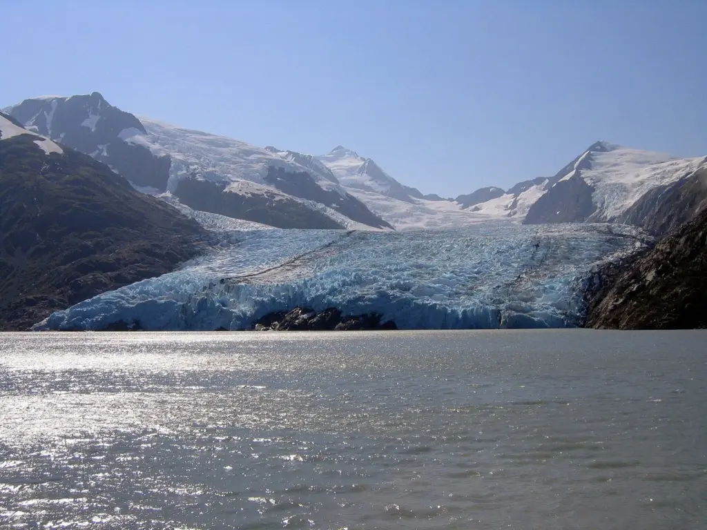 Portage Glacier's blue ice face across the water of Portage Lake below snowy peaks