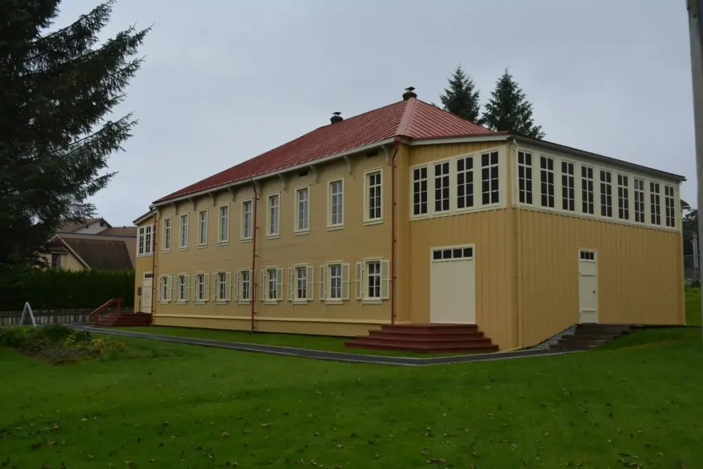 Two-story yellow Russian Bishop's House with a red roof and white-trimmed windows behind a lawn