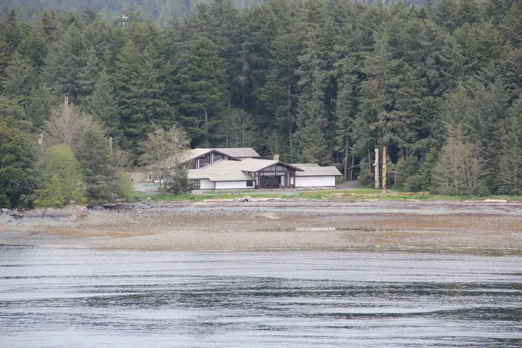 Low visitor center building and totem poles at the edge of the forest beside the shore at Sitka National Historical Park