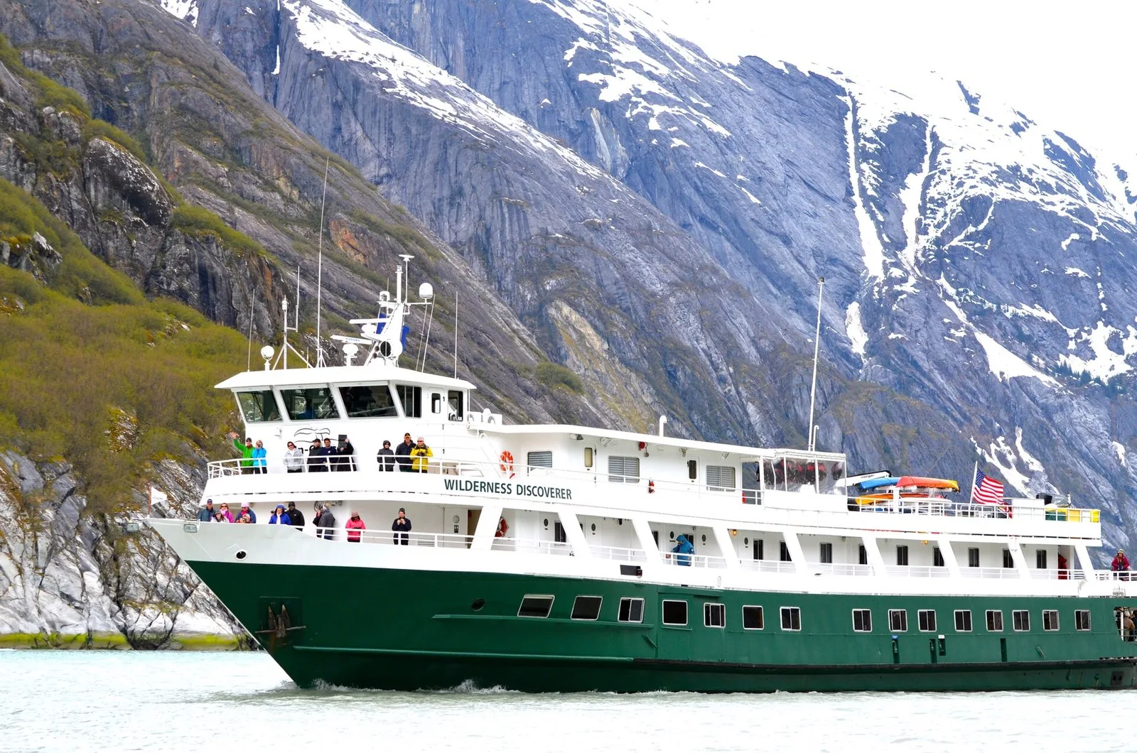 Small ship Alaska cruises use vessels like UnCruise's Wilderness Discoverer, seen below snowy granite walls with guests lining the rails