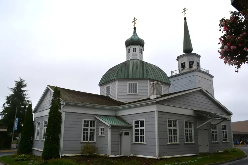 Gray wooden St. Michael's Cathedral with a green onion dome and bell tower on a downtown street corner