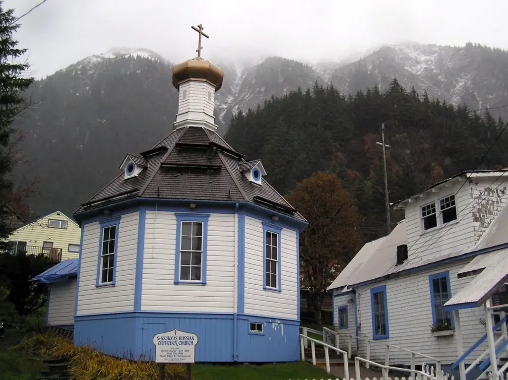 The small white octagonal St. Nicholas Russian Orthodox Church with a gold onion dome, set against misty forested mountains in Juneau