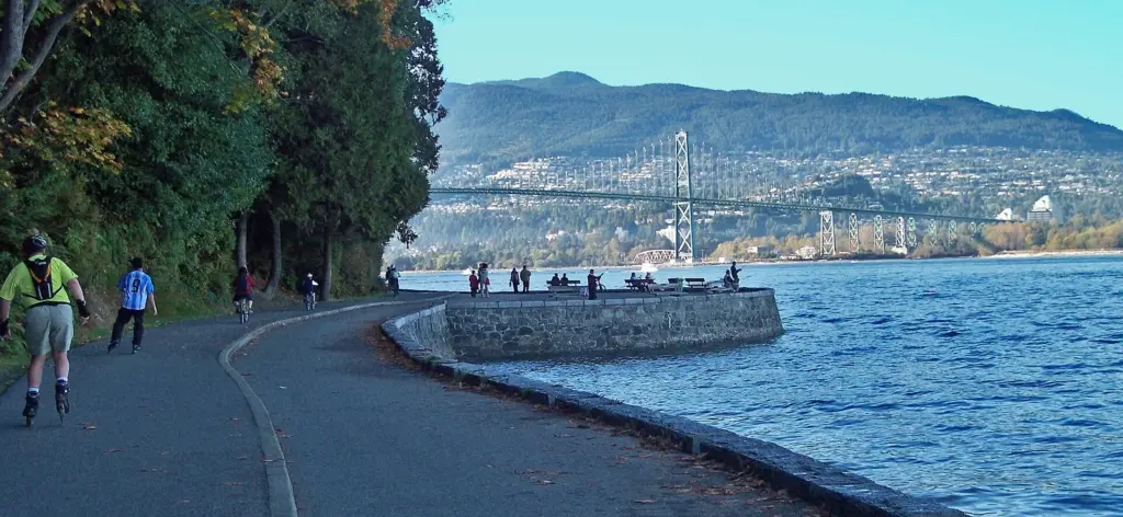 Walkers and cyclists on the Stanley Park seawall path with the Lions Gate Bridge across the water