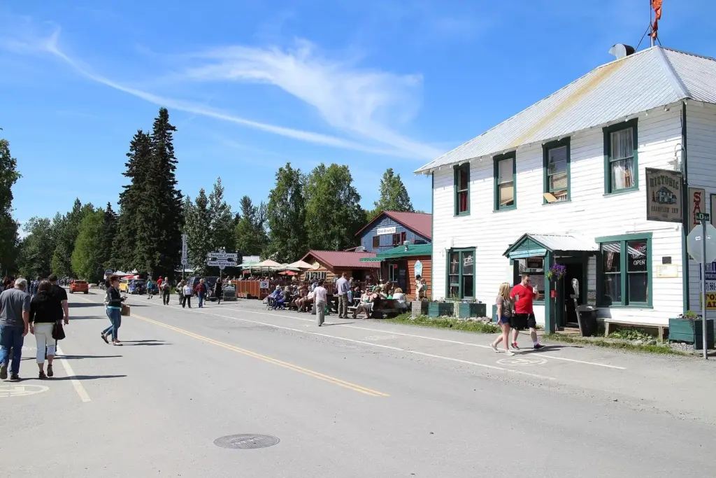Visitors walking along the main street of Talkeetna past historic wooden buildings on a sunny June day