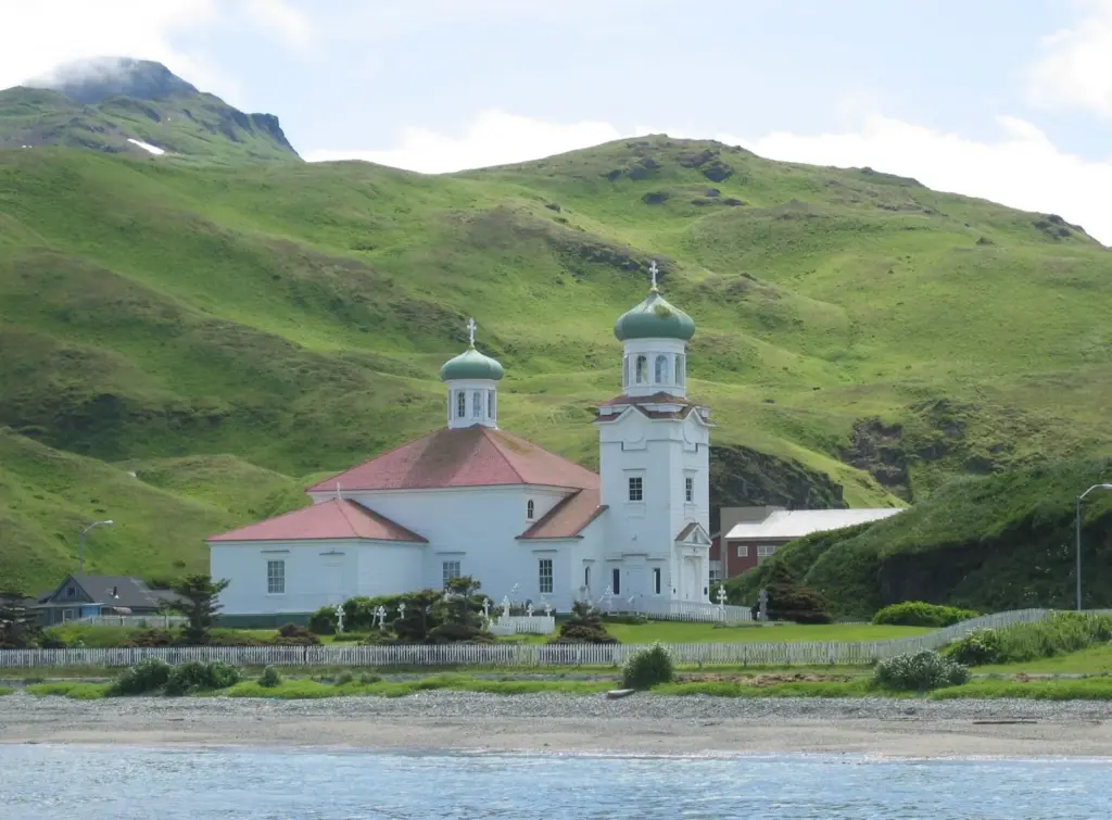 White Church of the Holy Ascension with green onion domes below grassy hills in Unalaska