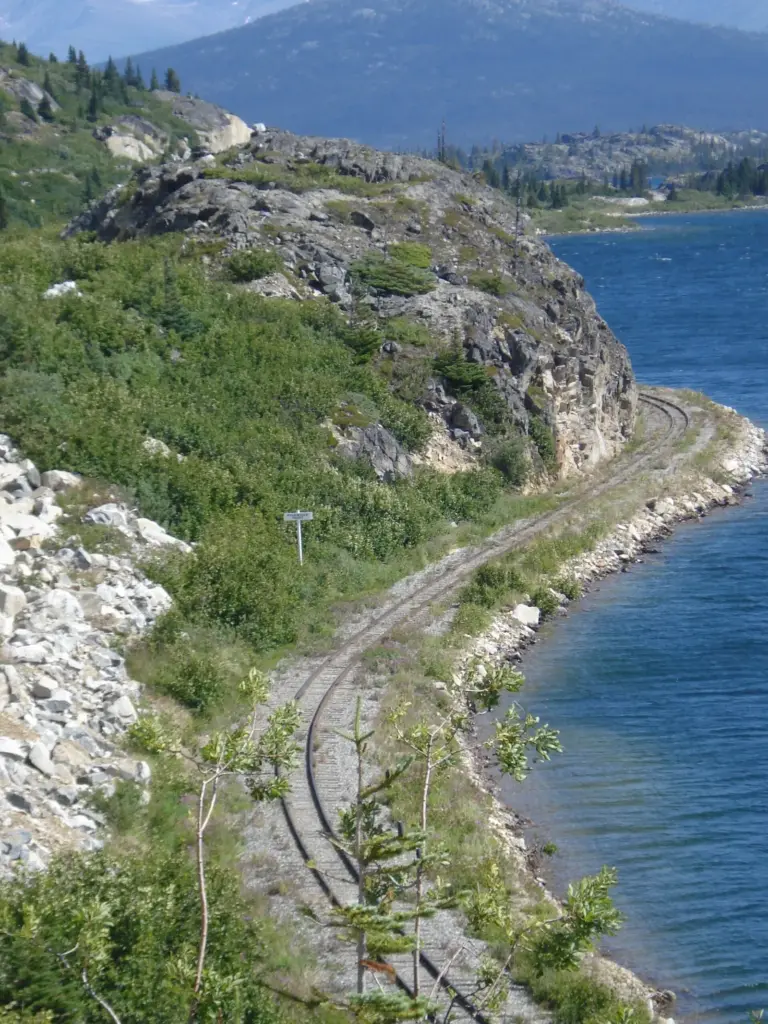 Railroad tracks curving along the rocky shore of a blue alpine lake near Fraser, British Columbia