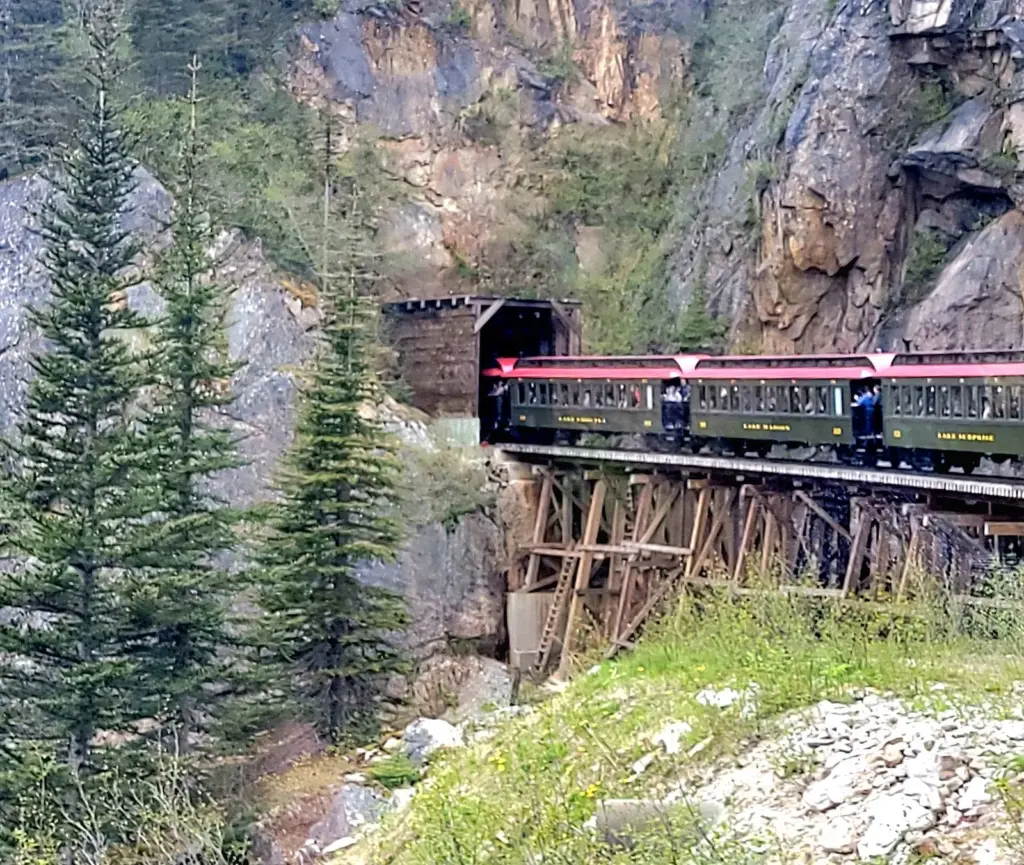 White Pass and Yukon Route passenger train crossing a wooden trestle into a rock tunnel north of Skagway